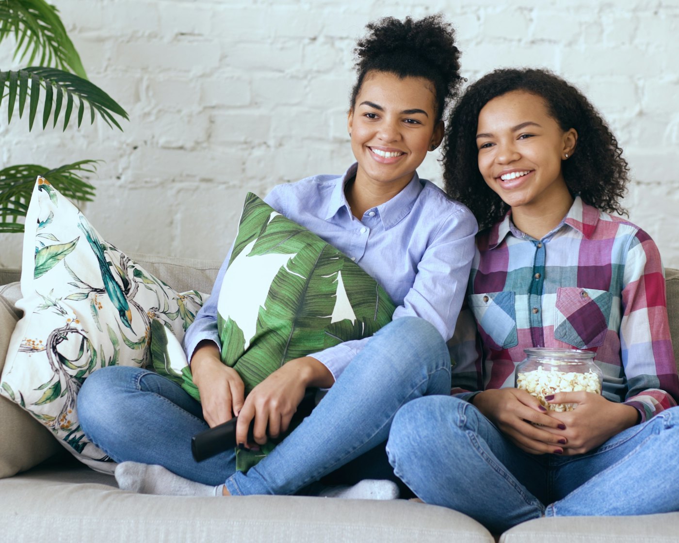 Two friends laughing together on a sofa, sharing a jar of popcorn