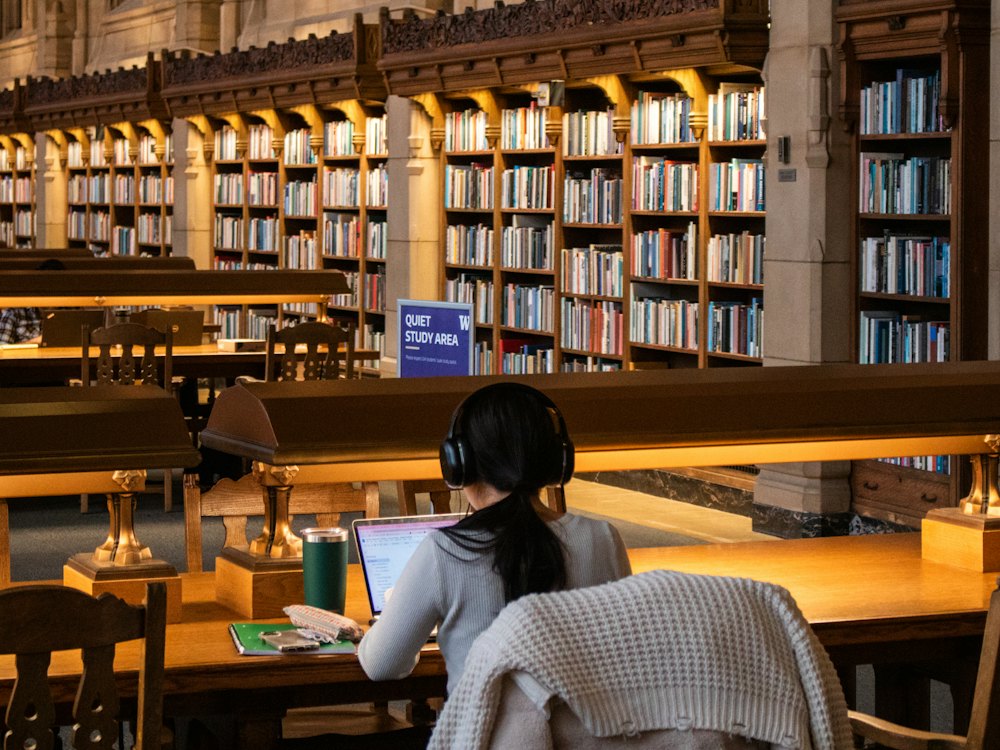 A student working at a lamp-lit desk in a wood-panelled library lined with books