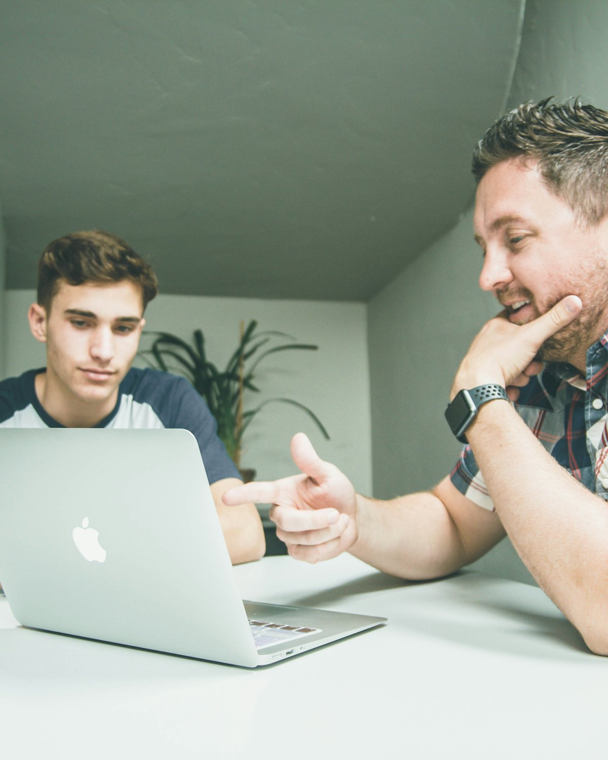 A teacher explaining a point to a teenage pupil working at a laptop