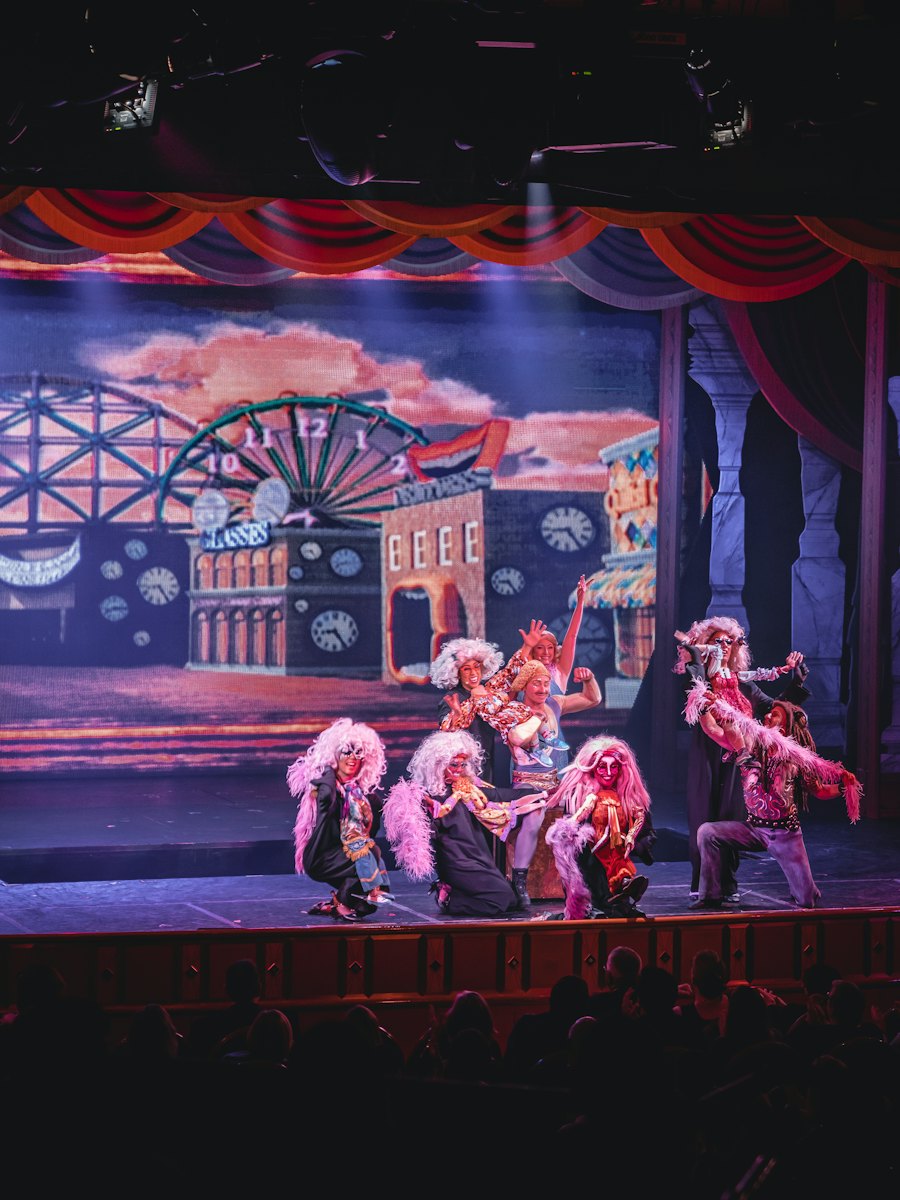 A cast in costume performing on a brightly painted stage set