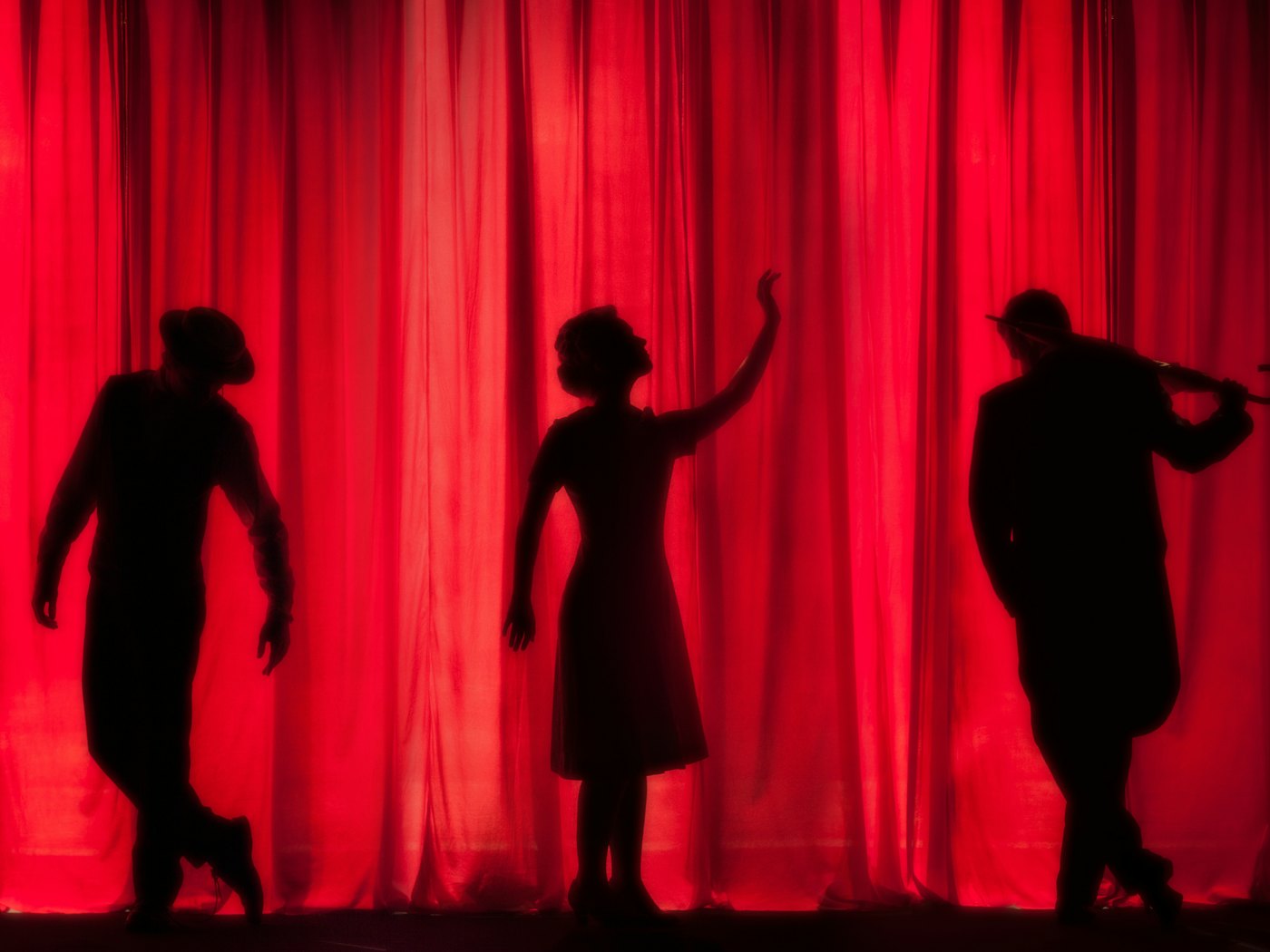 Three performers in silhouette against a glowing red stage curtain